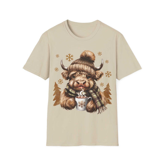 Beige t-shirt featuring a cozy Highland Cow wearing a knit hat and plaid scarf holding a hot chocolate mug with snowflakes.