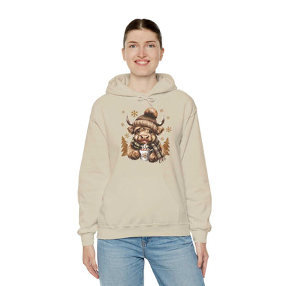 Woman wearing beige Highland Cow Hoodie with winter-themed cow holding hot chocolate in knit hat and plaid scarf design