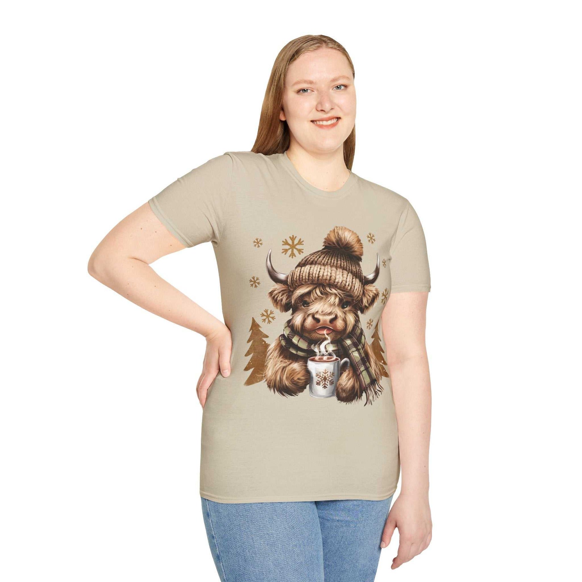 Woman wearing beige t-shirt with Highland Cow in winter hat and scarf holding hot chocolate design