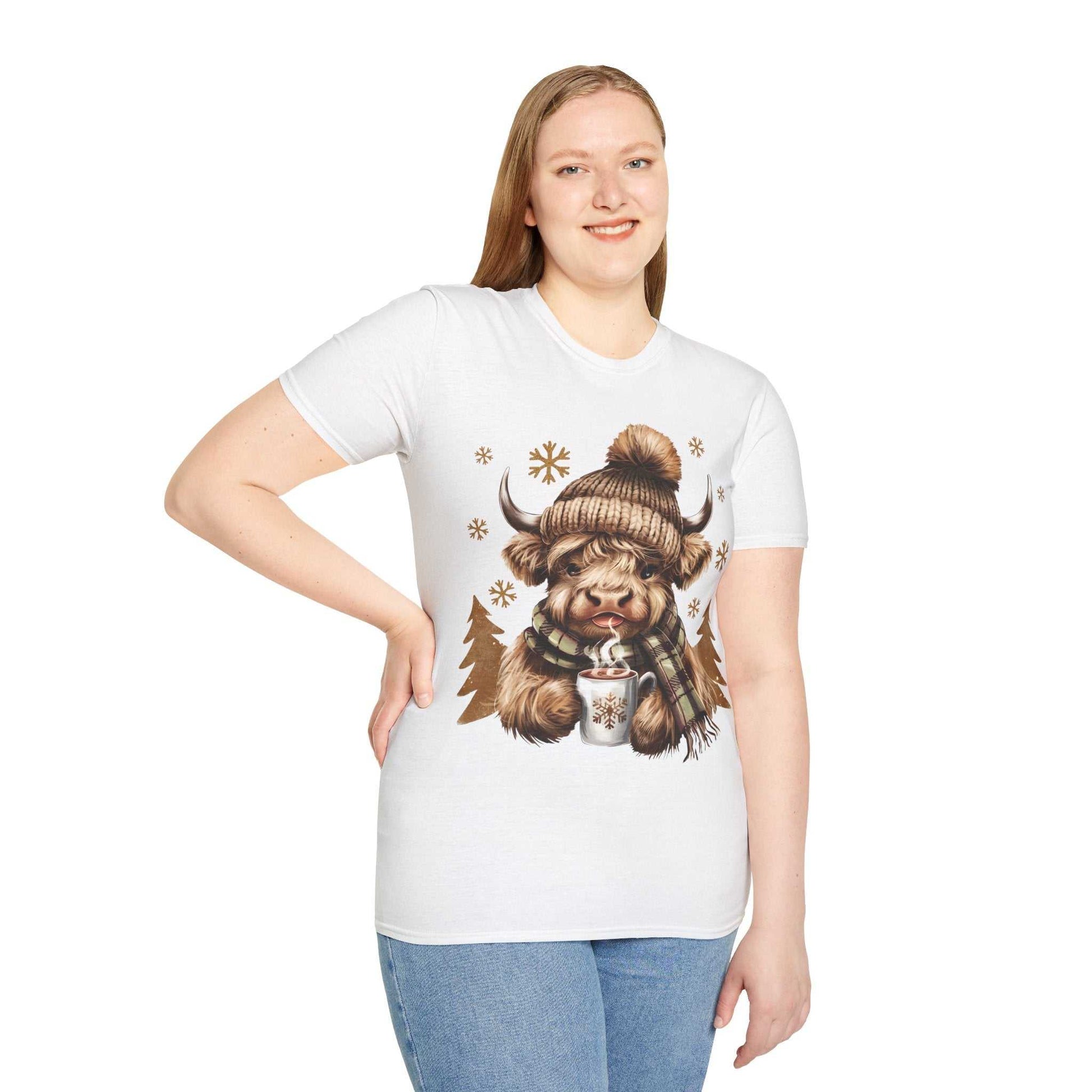 Woman wearing white Highland Cow t-shirt with cozy winter design of cow in knit hat holding hot chocolate