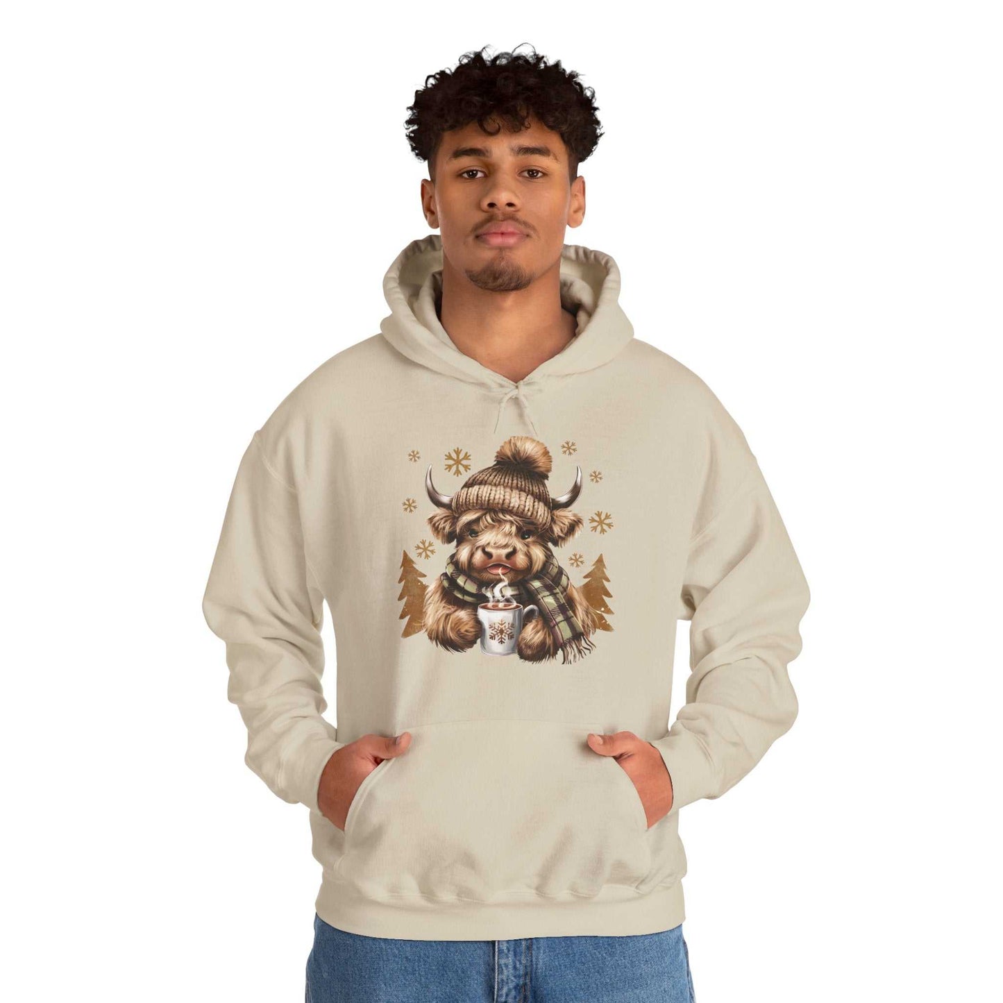 Man wearing beige Highland Cow Hoodie with cozy winter design of Highland cow in knit hat and scarf holding hot chocolate mug