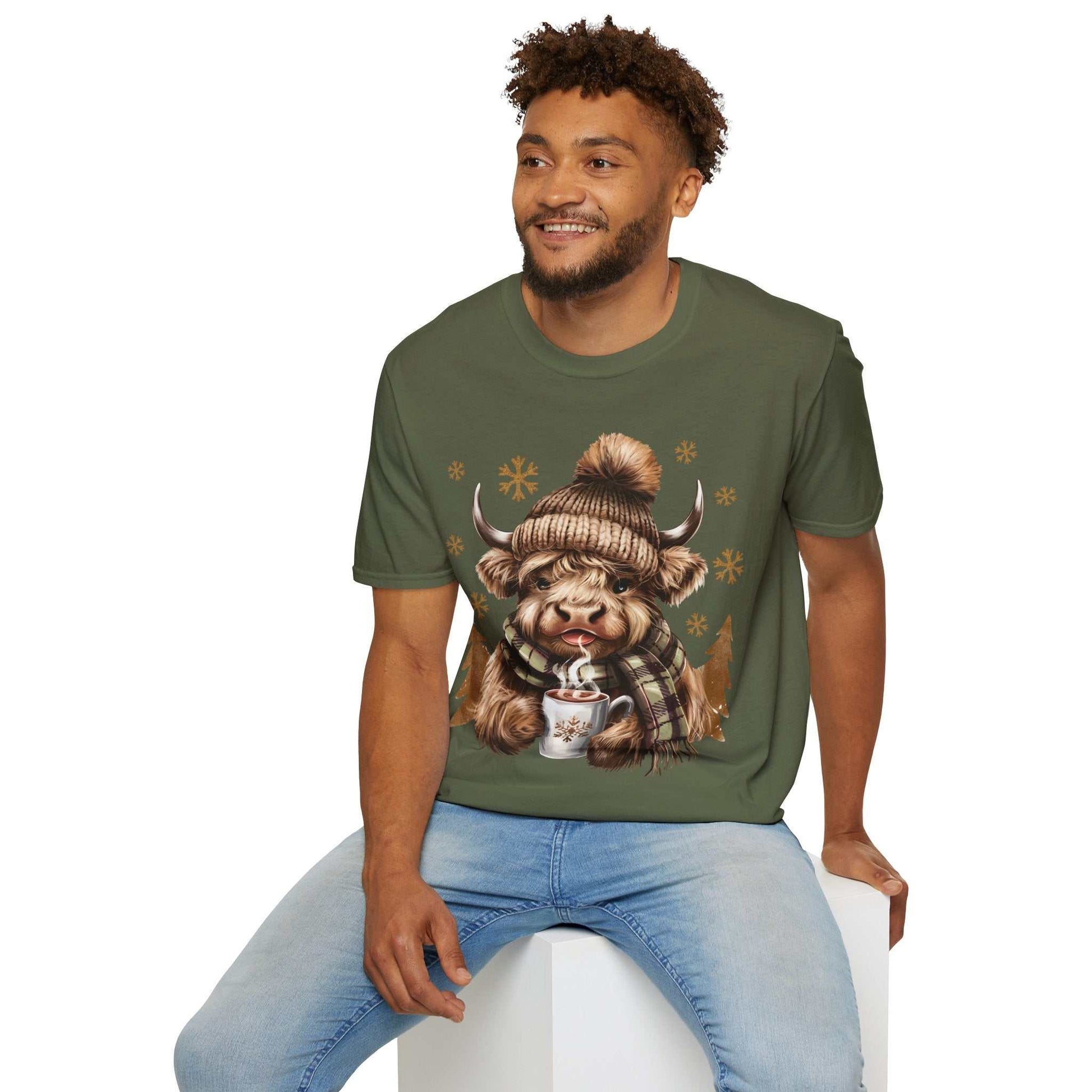 Man wearing Highland Cow t-shirt with winter hat, scarf, and hot chocolate design on green cotton tee