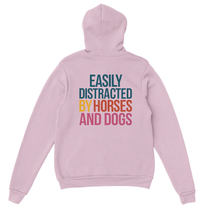 Light pink hoodie with "Easily Distracted by Horses and Dogs" text on back in colorful letters, cozy cotton-poly blend fabric.