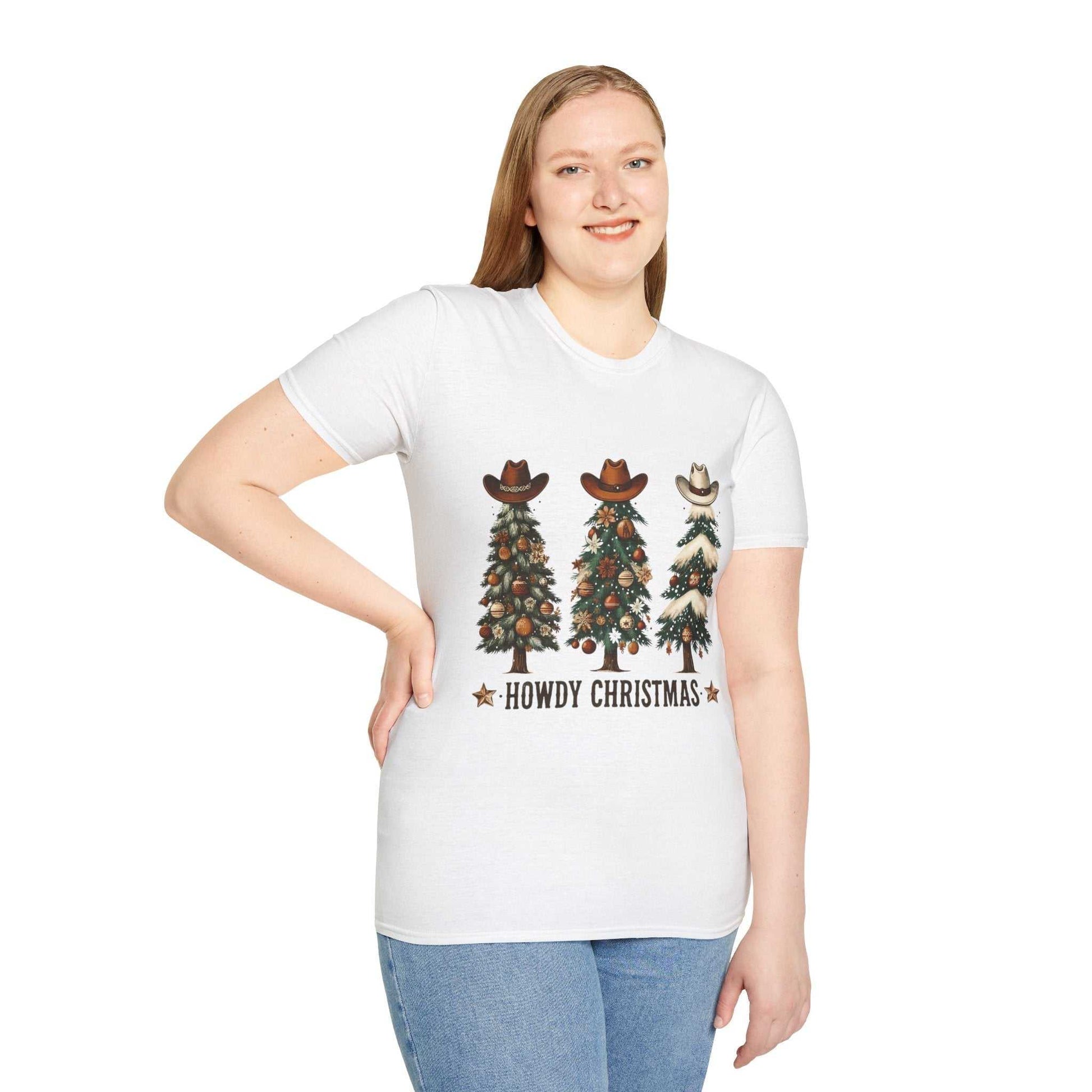 Woman wearing white Howdy Christmas Cowboy Tree T-shirt with decorated Christmas trees topped with cowboy hats and text "Howdy Christmas"