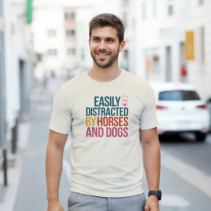 Man wearing Easily Distracted By Horses and Dogs T-Shirt with colorful text on a casual street background