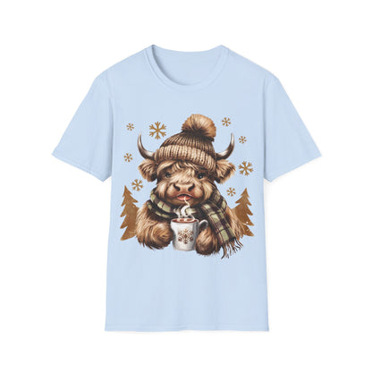 Light blue t-shirt featuring a cozy Highland Cow wearing a knit hat and scarf, holding a hot chocolate cup with snowflakes.
