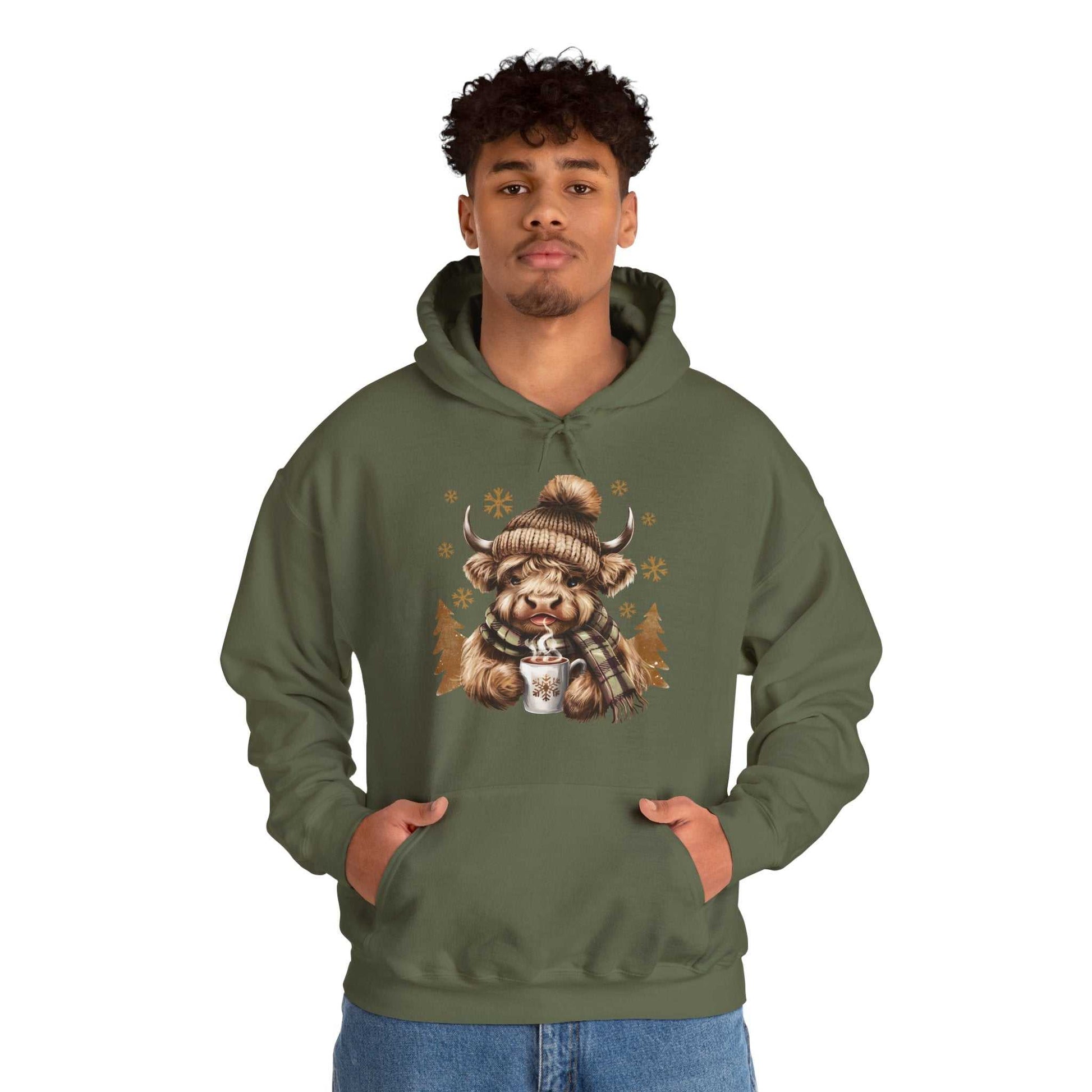 Man wearing olive green Highland Cow Hoodie with winter-themed cow holding hot chocolate illustration