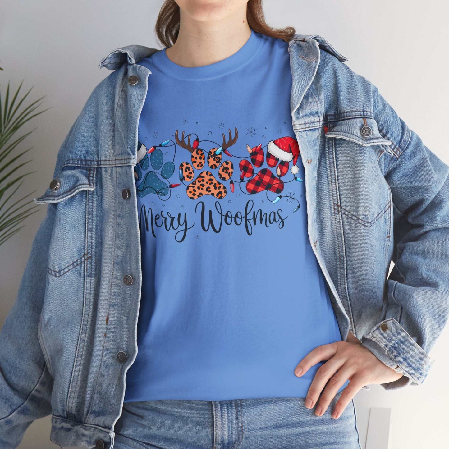 Merry Woofmas Christmas tee with festive paw prints in plaid, leopard, Santa hats, and antlers on blue cotton shirt worn with denim jacket