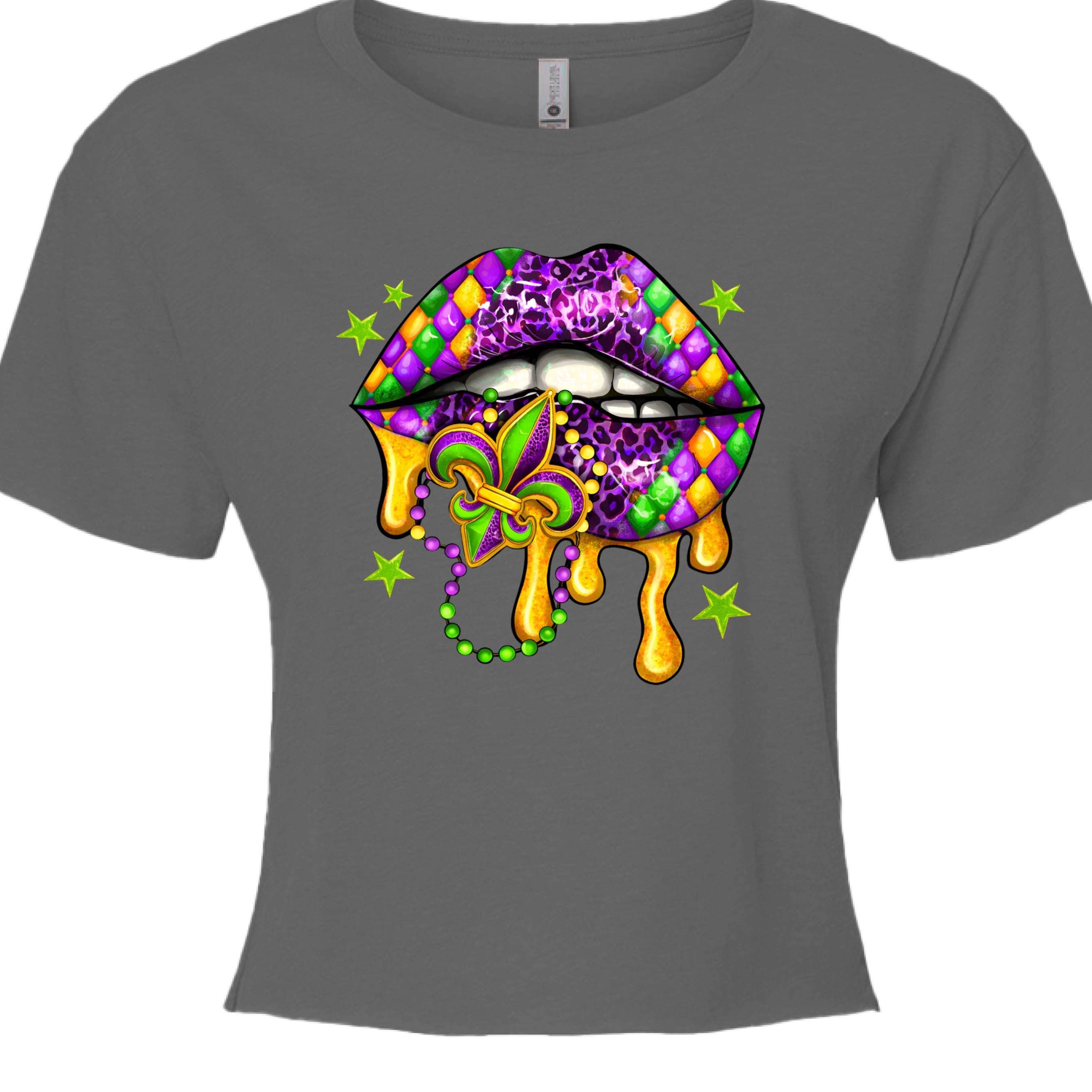 A charcoal grey, cropped Mardi Gras Lips Baby Tee featuring a large, vibrant graphic of a pair of lips decorated in Mardi Gras themes. The top lip features a purple, gold, and green diamond harlequin pattern, while the bottom lip has a purple leopard print. Gold liquid "drips" from the mouth, which holds a decorative Fleur-de-lis and a string of Mardi Gras beads. 