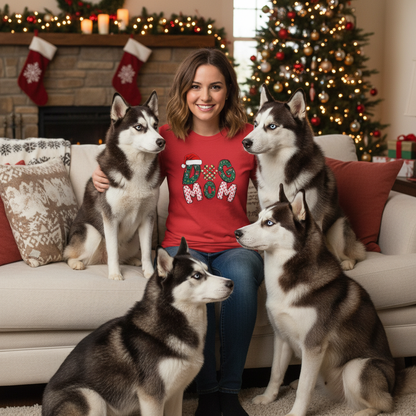 Woman wearing red Christmas Dog Mom Tee with festive design sitting on couch with four husky dogs in holiday decorated living room