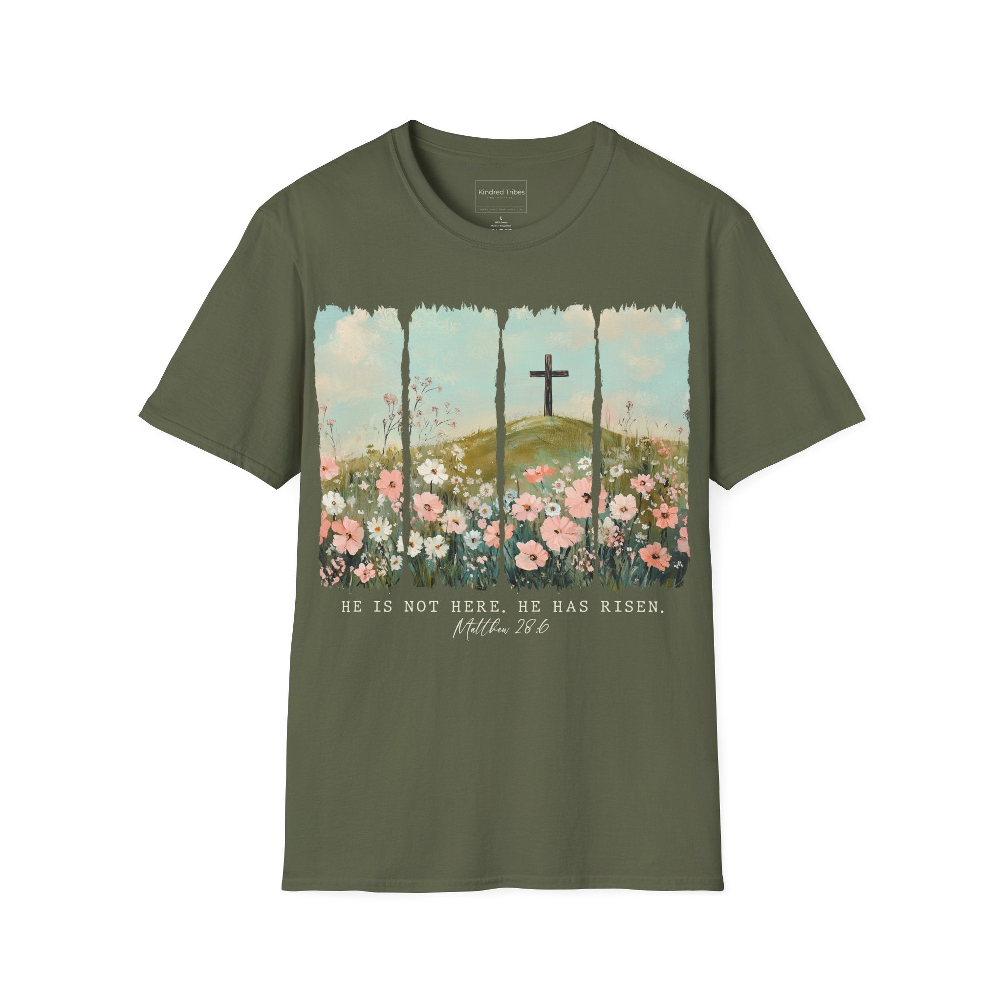 Military Green Easter He Has Risen - Floral Cross Christian Tee featuring a painterly, four-panel graphic of a serene spring landscape. A wooden cross stands on a green hilltop overlooking a field of pink, white, and red wildflowers under a soft blue sky. Below the artwork, the text reads 'HE IS NOT HERE. HE HAS RISEN.' followed by the scripture 'Matthew 28:6' in elegant cursive.