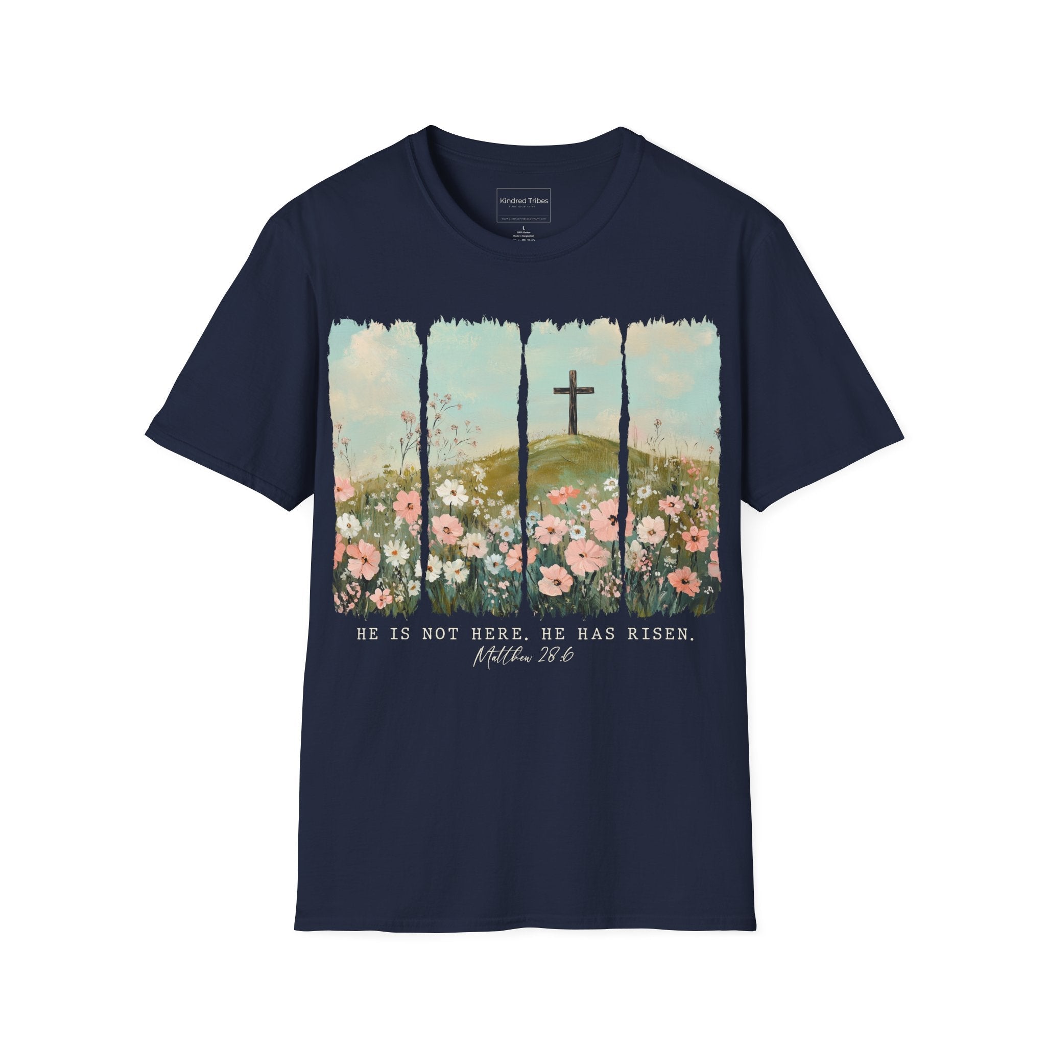 Navy Blue Easter He Has Risen - Floral Cross Christian Tee featuring a painterly, four-panel graphic of a serene spring landscape. A wooden cross stands on a green hilltop overlooking a field of pink, white, and red wildflowers under a soft blue sky. Below the artwork, the text reads 'HE IS NOT HERE. HE HAS RISEN.' followed by the scripture 'Matthew 28:6' in elegant cursive.