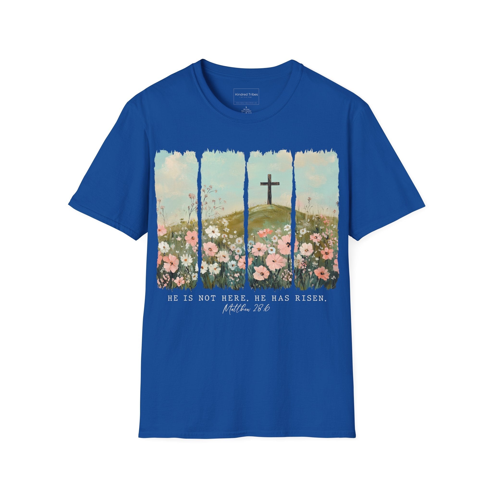 Royal Blue Easter He Has Risen - Floral Cross Christian Tee featuring a painterly, four-panel graphic of a serene spring landscape. A wooden cross stands on a green hilltop overlooking a field of pink, white, and red wildflowers under a soft blue sky. Below the artwork, the text reads 'HE IS NOT HERE. HE HAS RISEN.' followed by the scripture 'Matthew 28:6' in elegant cursive.