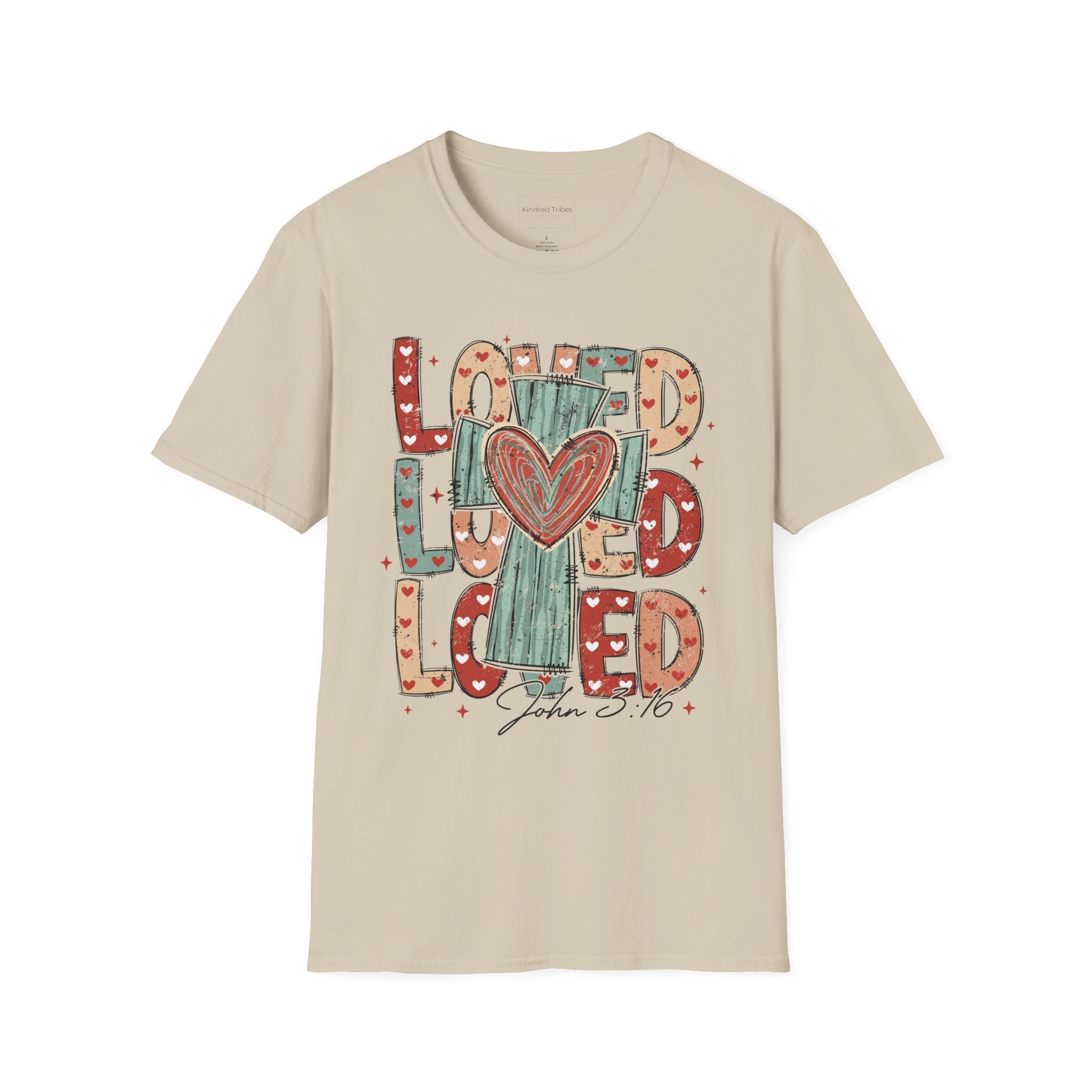 Beige Loved Cross Heart T-Shirt featuring a large, colorful graphic on the front. The design consists of the word "LOVED" repeated three times in a stacked, chunky block font. The letters are filled with various patterns, including solid colors, stripes, and small hearts in shades of red, sage green, and tan. In the center of the text is a distressed, teal-colored cross with a large, hand-drawn red heart layered over the middle. Below the main graphic, the scripture reference "John 3:16" is written.