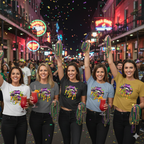 Five women celebrating Mardi Gras on Bourbon Street.  Each woman is wearing the Mardi Gras Lips T-shirt featuring a large, vibrant graphic of a pair of lips decorated in Mardi Gras themes. The top lip features a purple, gold, and green diamond harlequin pattern, while the bottom lip has a purple leopard print. Gold liquid "drips" from the mouth, which holds a decorative Fleur-de-lis and a string of Mardi Gras beads. 